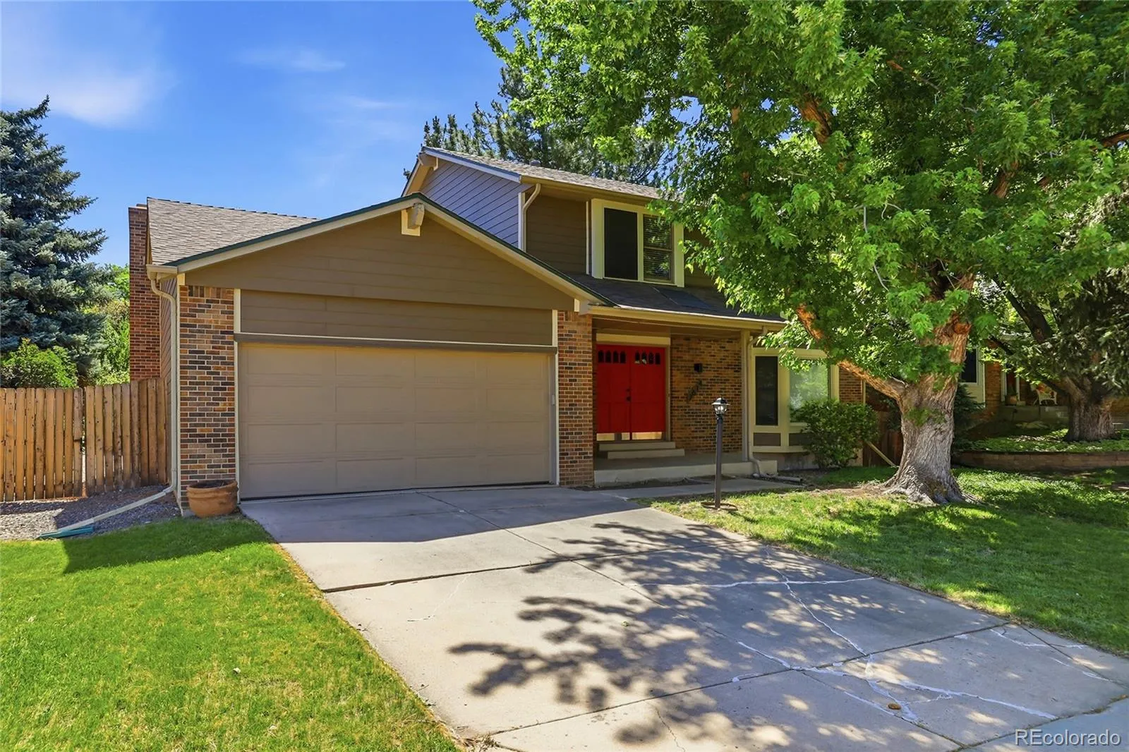 Two-story brick and siding home with red double front doors beneath a mature shade tree, 7614 South Emerson Circle, Centennial