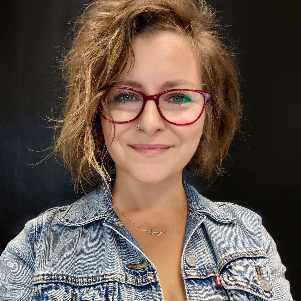 Varvara Lytkina, smiling, in a denim jacket and red glasses