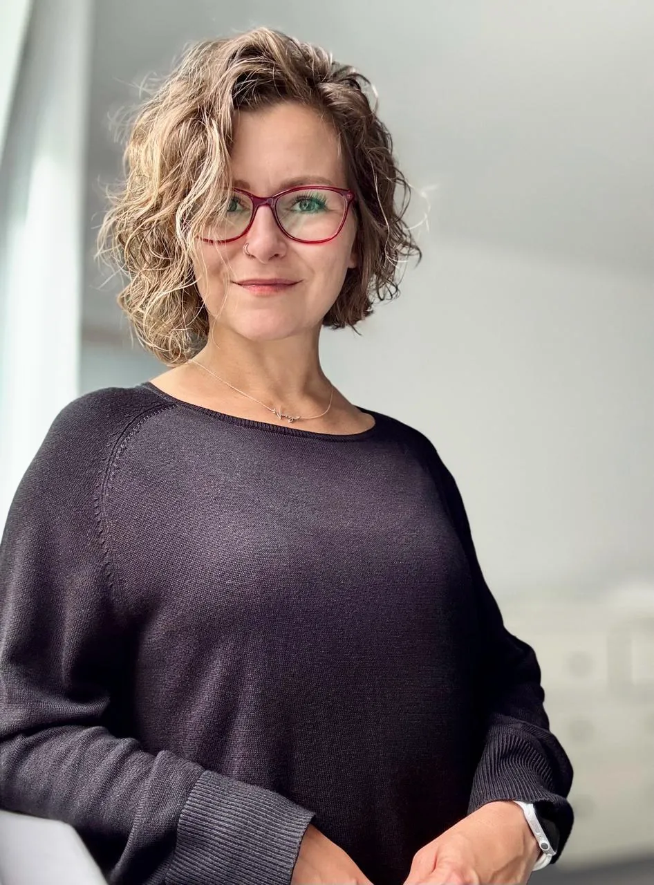 Varvara Lytkina in a dark sweater and red glasses, photographed indoors in soft natural light